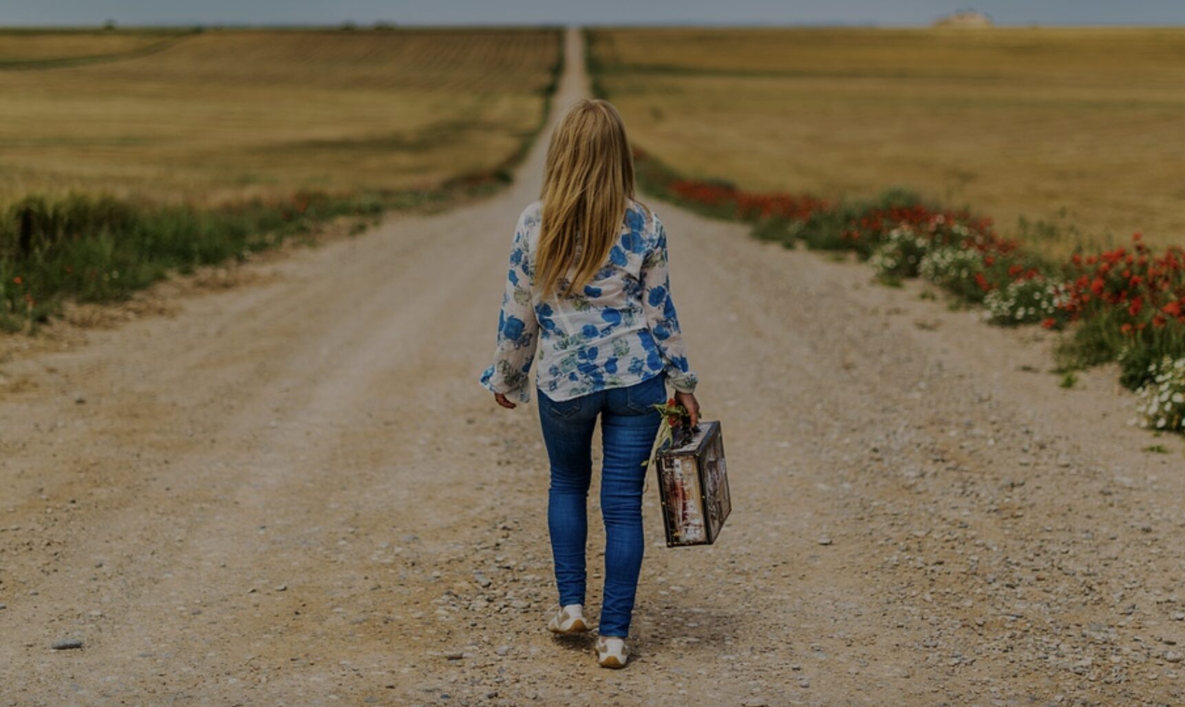 woman walking alone down the middle of a road , in the countryside just fields